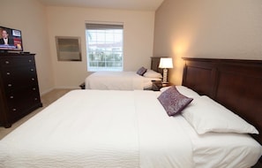 Een hotelkamer met twee bedden, een dressoir, een televisie en een raam met jaloezieën.