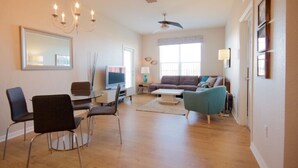 A modern living room with a glass dining table, black chairs, a sofa, and a teal armchair.
