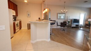 A modern kitchen with a central island, wooden cabinets, and a dining area with a TV and seating.