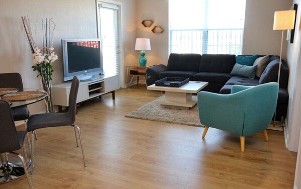 Ein modernes Wohnzimmer mit Flachbildfernseher, einer Couch, einem Couchtisch und einem Essbereich mit Stühlen.