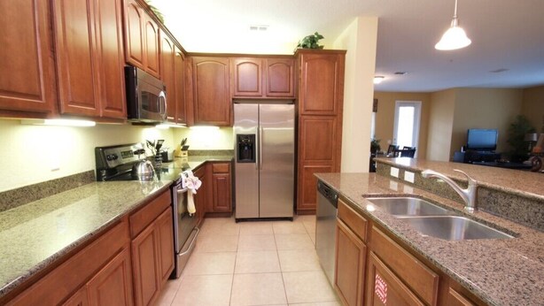 A kitchen with wooden cabinets, granite countertops, stainless steel appliances, and a double sink. - 12-103 3 Bedroom Home by RedAwning (Orlando)