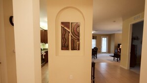 A spacious hallway with a kitchen area on the left, a dining area with chairs, and a door leading to another room. - 12-103 3 Bedroom Home by RedAwning (Orlando)