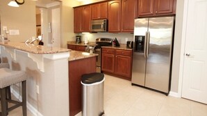 A kitchen with wooden cabinets, stainless steel appliances, a granite countertop, and a trash can. - 10-106 2 Bedroom Condo by RedAwning (Orlando)