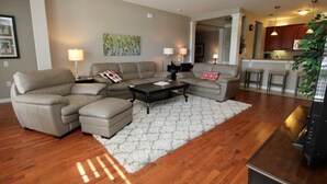 A living room with a sectional sofa, a coffee table, and a rug. There is a kitchen area visible in the background. - 10-106 2 Bedroom Condo by RedAwning (Orlando)