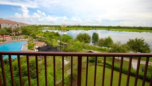 A view of a swimming pool surrounded by lush greenery and a calm lake, with a clear sky above.