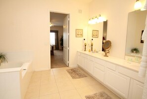 Une salle de bain avec une baignoire, un meuble-lavabo avec un miroir et une porte donnant sur une autre pièce.
