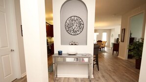 Een hal met een witte console tafel, een decoratief wandobject en een eethoek op de achtergrond.