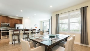 A spacious kitchen with modern appliances, a dining area with a glass table and chairs, and large windows offering a view of the outdoors.