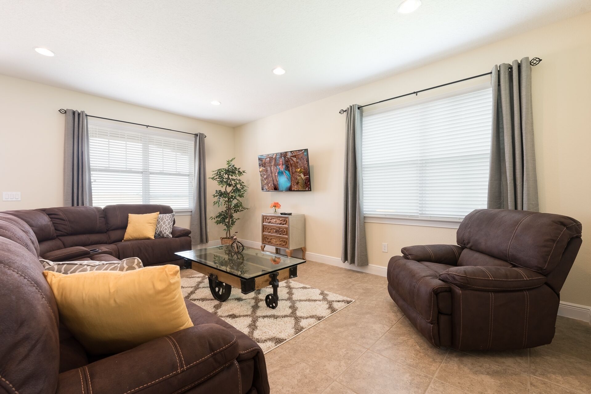 A living room with a brown leather sofa, a brown leather armchair, a glass coffee table, and a potted plant.