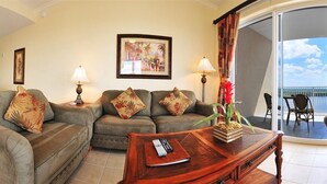 A living room with a sofa set, two lamps, a painting, and a view of the balcony.