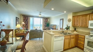 A modern kitchen with wooden cabinets, a dishwasher, an oven, and a dining area with a glass table and chairs.