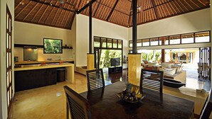 A spacious living area with a high ceiling, a dining table with chairs, a kitchen area with a TV, and large windows allowing natural light. - Two Bedrooms Villa With Private Pool, Large Landscape Garden and Kitchen (Karangasem)
