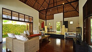 A spacious living area with a high ceiling, wicker furniture, a wooden floor, and large windows offering a view of greenery. - Two Bedrooms Villa With Private Pool, Large Landscape Garden and Kitchen (Karangasem)