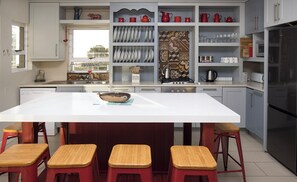 Uma cozinha moderna com ilha central, banquetas de bar e diversos utensílios de cozinha.