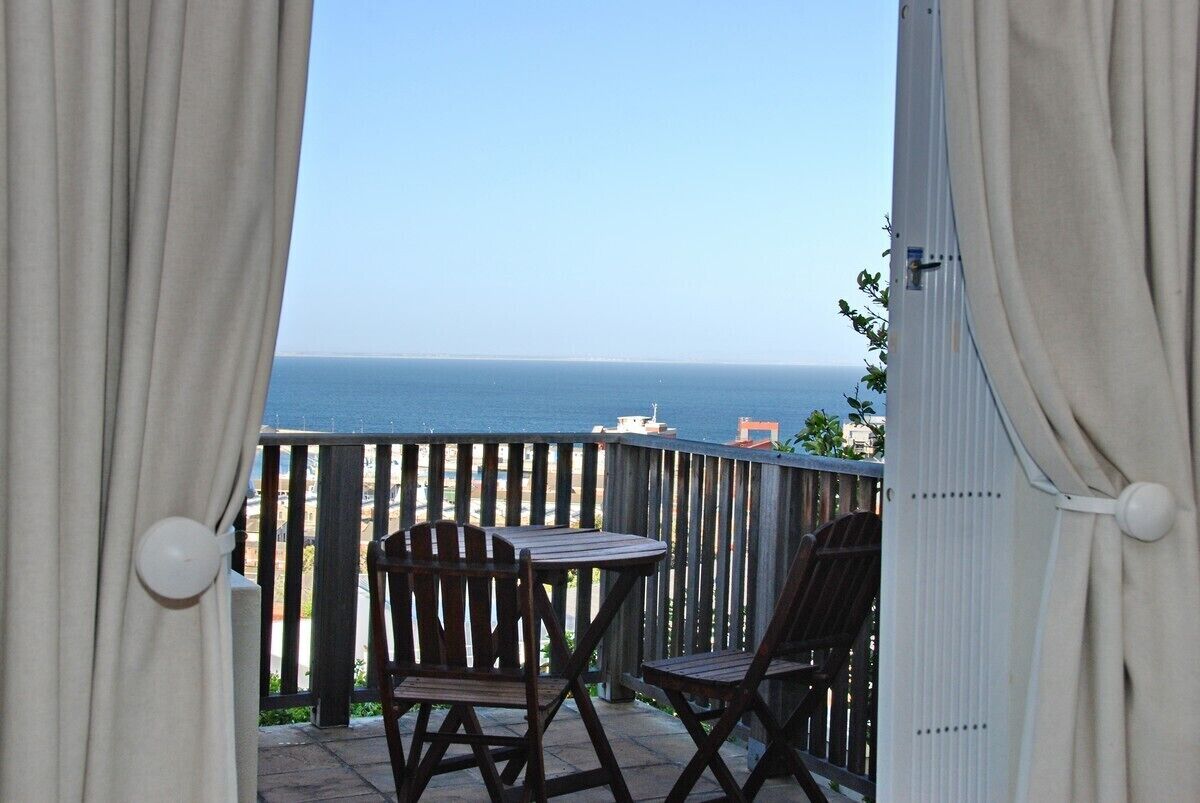 A balcony with two wooden chairs and a table, overlooking a body of water.