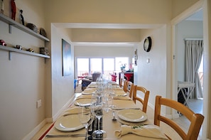 A dining room with a long table set for a meal, chairs, and a kitchen area in the background.
