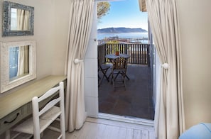 A room with a desk, chair, and a view of a balcony with a table and chairs.