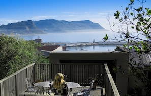 A balcony with a table and chairs, overlooking a body of water and distant mountains.