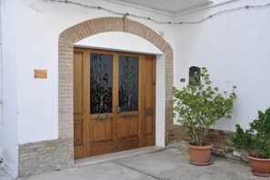 Una puerta de madera con paneles de vidrio decorativos, un arco de ladrillo y plantas en macetas.