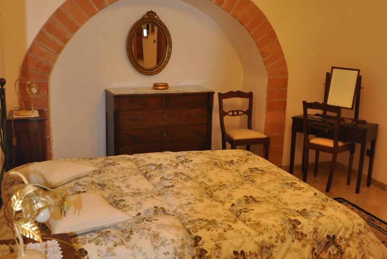 Une chambre avec une couvre-lit à motifs floraux, une commode en bois, un miroir et une chaise.