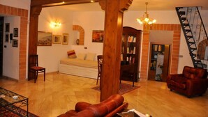 Ein geräumiges Wohnzimmer mit einer Couch, roten Ledersesseln, einem Holzregal und einer Treppe.