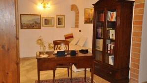 Ein Zimmer mit Schreibtisch aus Holz, einem Stuhl, einem Bücherregal und einem Bett mit gemustertem Teppich.