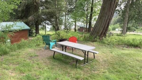 Une table de pique-nique avec des bancs, installée dans un espace herbeux bordé d’arbres.