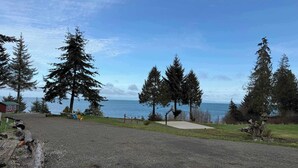A gravel parking area with a view of the sea and tall trees. - Ocean View Tent Site T3 (Port Angeles)