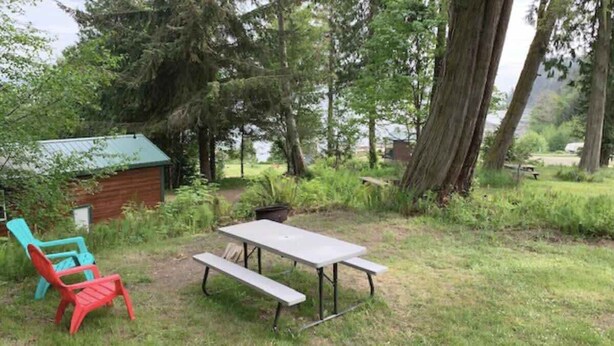 A picnic table with benches in a grassy area with trees and a small shed in the background. - Ocean View Tent Site T3 (Port Angeles)