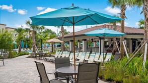 A poolside area with lounge chairs, umbrellas, and a tiled walkway.