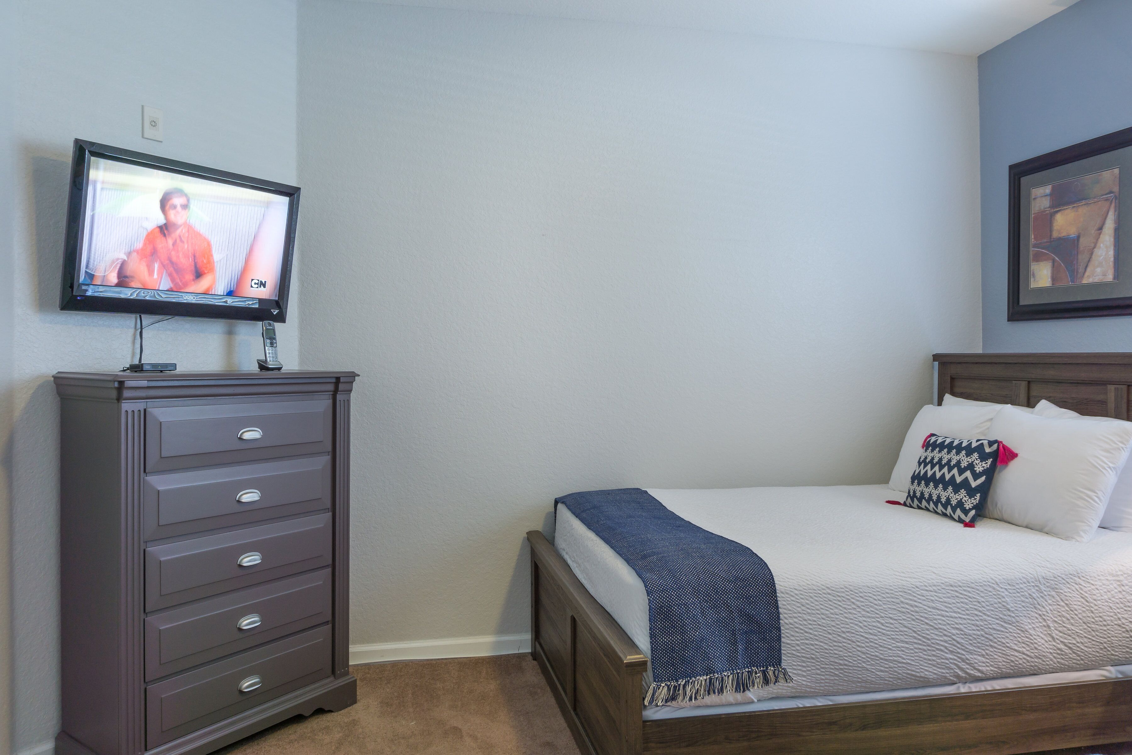 A bedroom with a bed, a dresser, a television, and a framed picture on the wall.