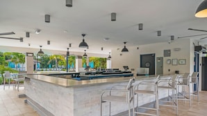 A modern bar area with a long counter, multiple bar stools, and pendant lighting.
