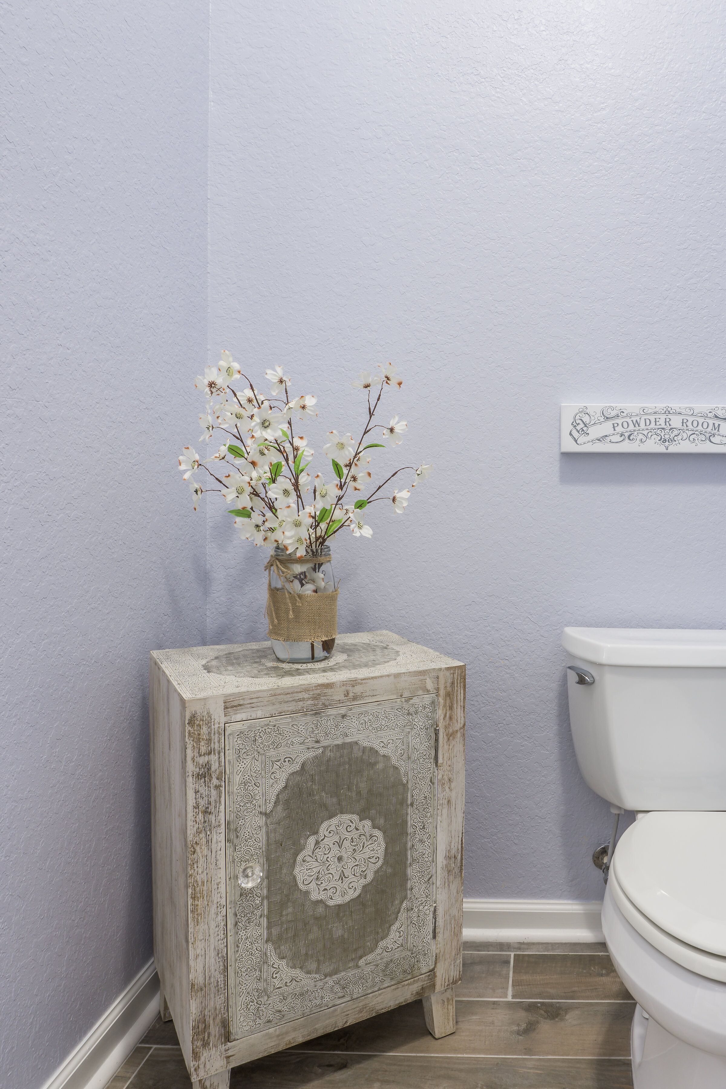 A bathroom with a rustic wooden cabinet, a white toilet, and a wall-mounted sign.