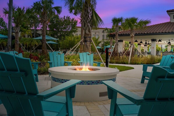 A fire pit surrounded by turquoise chairs in an outdoor setting with palm trees and a building in the background. - Casa Toscana Deluxe 3 Bedroom Condo by RedAwning (Orlando)