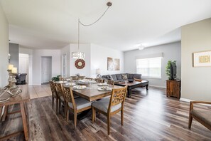 A spacious living room with a dining area, wooden flooring, and a large window providing natural light. - Casa Toscana Deluxe 3 Bedroom Condo by RedAwning (Orlando)