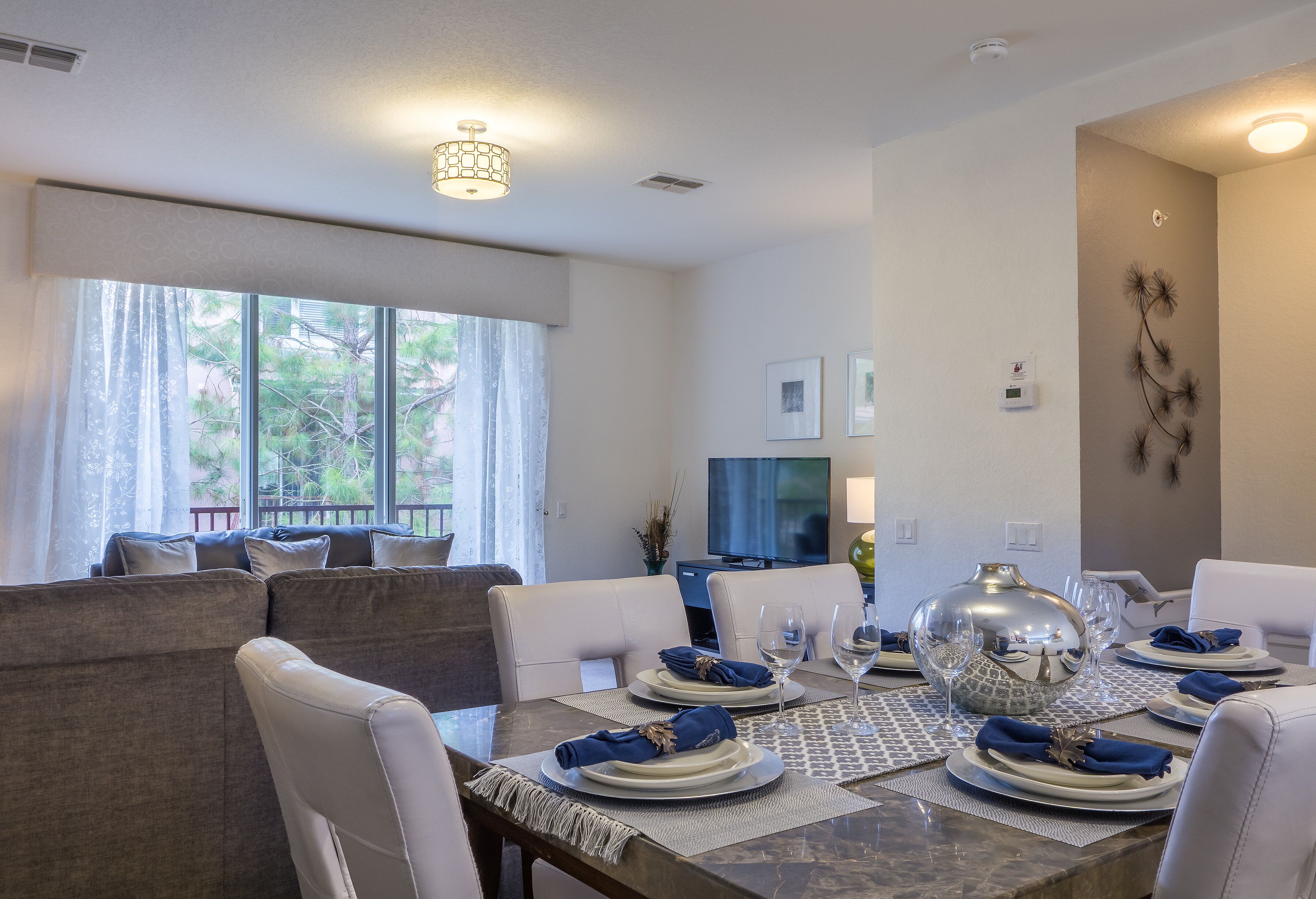 Un comedor con una mesa dispuesta para seis personas, un sofá y un televisor al fondo.