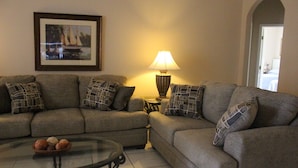 A living room with a sofa set, a glass coffee table, a lamp, and a framed picture on the wall. - Little Mermaid Villa- Beautiful Private Villa (Haines City)