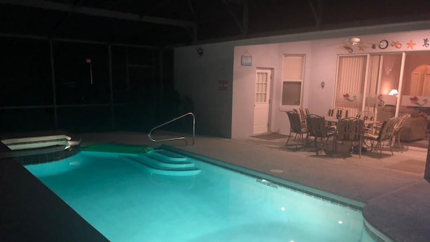 An indoor swimming pool with a clear water edge, a diving board, and a seating area with chairs and a table. - Little Mermaid Villa- Beautiful Private Villa (Haines City)