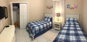 A bedroom with two beds, a wardrobe, a bedside table, and a lamp.