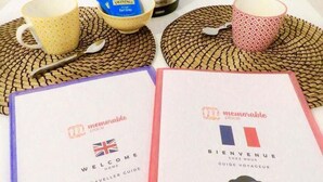 To rejsegidser med titlerne "Welcome Home" og "Bienvenue Chez Nous", et WiFi-symbol, en elkedel og to kopper på et bord.
