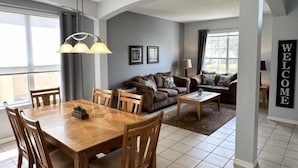 Un vaste espace de vie comprenant une table à manger et des chaises, un canapé et un panneau mural sur lequel est inscrit « BIENVENUE ».