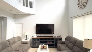 Un salon spacieux doté d’un grand téléviseur à écran plat, de deux canapés gris, d’une table basse et d’un ventilateur de plafond.