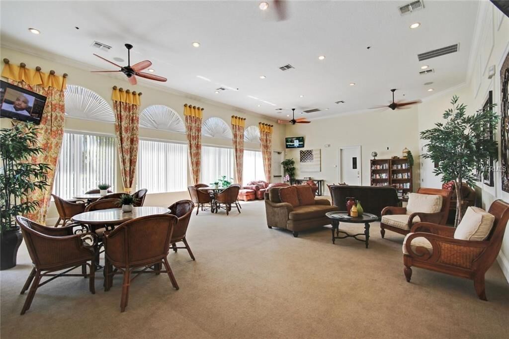 A spacious living room with a round dining table, several sofas, and a coffee table. There are ceiling fans, a TV, and a bookshelf.