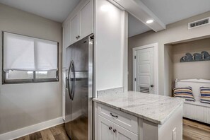 Una cocina moderna con armarios blancos, un refrigerador de acero inoxidable, una encimera de mármol y un banco empotrado con cojines a rayas.