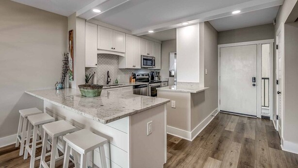 Una cocina moderna con armarios blancos, una isla central con taburetes de bar, microondas y refrigerador.