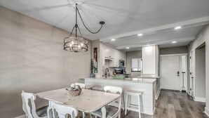 Una cocina moderna con armarios blancos, una isla central y un comedor con mesa y sillas blancas.
