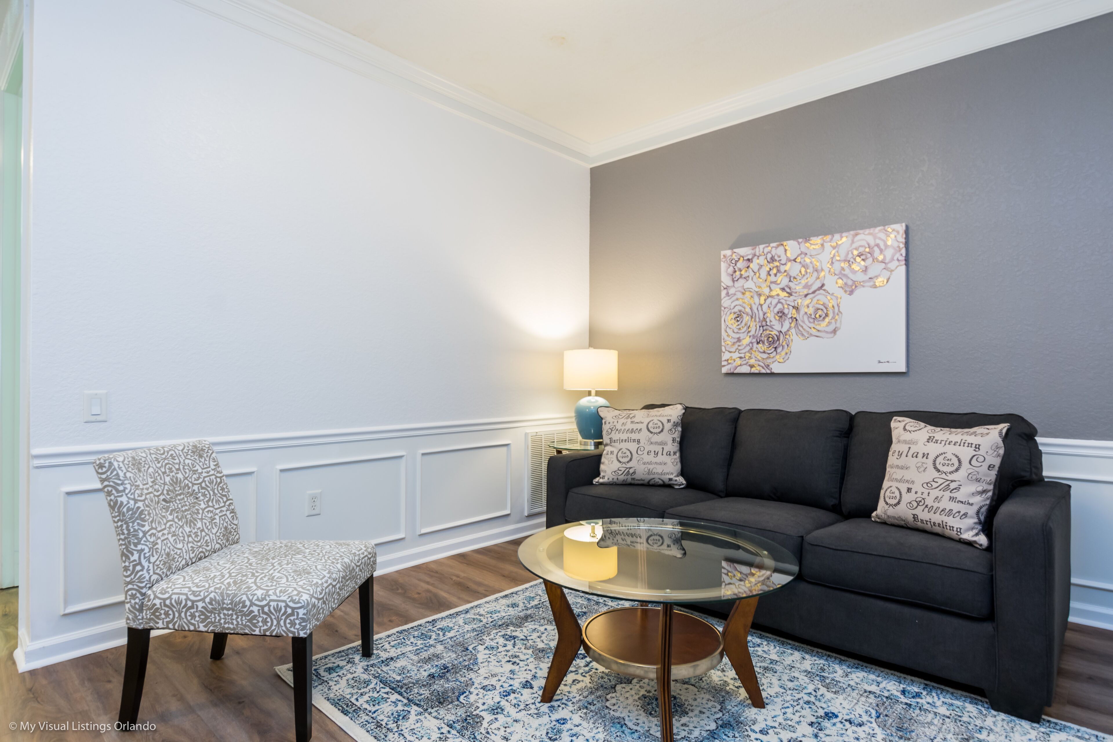 Un salon avec un canapé gris foncé, un fauteuil à motifs et une table basse en verre.