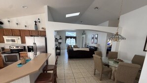 Una cocina moderna con una isla central, comedor con sillas y sala de estar con sofá y televisor.