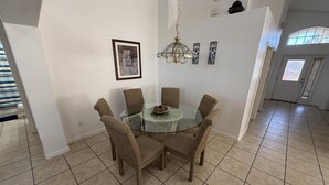 Un comedor con una mesa redonda de vidrio, seis sillas, una araña y un cuadro en la pared.