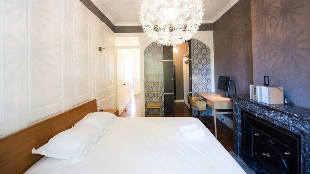 Ein Hotelzimmer mit einem großen Bett, einem Schreibtisch mit Computer, einer modernen Deckenleuchte und einem Badezimmer mit Musterwand.